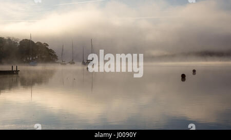 Nebel steigt um Boote vertäut am Lake Windermere in Ambleside in Englands Lake District National Park. Stockfoto