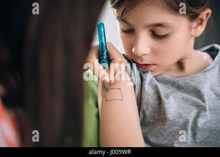 Mädchen schreiben Tattoo auf Arm ihrer Freundin mit Stift Stockfoto