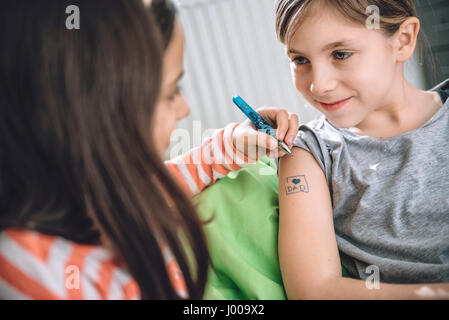 Mädchen schreiben Tattoo auf Arm ihrer Freundin mit Stift Stockfoto