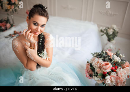 Erstaunliche Brünette Braut malte Mehendi im Hochzeitskleid sitzt auf dem Bett im Hintergrund die schöne Innenausstattung. Stockfoto