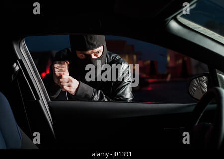 Männliche Carjacker mit Haube auf dem Kopf versucht Autotür mit Schraubenzieher zu öffnen. Fahrzeug entriegeln Dieb. Auto Verkehr Kriminalität Stockfoto