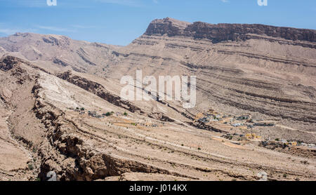 Dorf eingebettet in die trockenen Berge von Wadi Bani Khalid, Sultanat von Oman, traditionelle Architektur und zerklüftete Wüstenlandschaft, heißes Klima Stockfoto