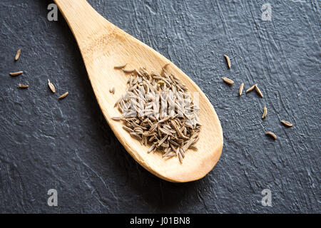 Kümmel. Schließen Sie herauf Bild Kreuzkümmelsamen (Zira) auf rustikalen Holzlöffel und schwarzen Hintergrund. Stockfoto