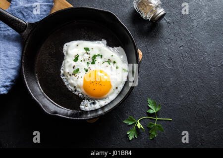 Spiegelei. Nahaufnahme der das Spiegelei auf einer Pfanne. Gesalzene und gewürzte Spiegelei mit Petersilie auf gusseisernen Pfanne und schwarzen Hintergrund. Stockfoto