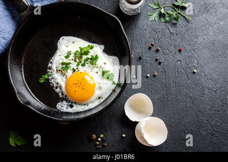 Spiegelei. Nahaufnahme der das Spiegelei auf einer Pfanne. Gesalzene und gewürzte Spiegelei mit Petersilie auf gusseisernen Pfanne und schwarzen Hintergrund. Stockfoto