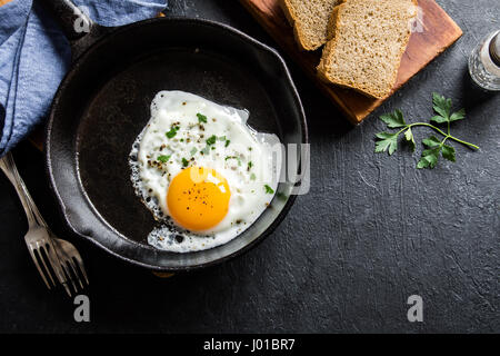 Spiegelei. Nahaufnahme der das Spiegelei auf einer Pfanne. Gesalzene und gewürzte Spiegelei mit Petersilie auf gusseisernen Pfanne und schwarzen Hintergrund. Stockfoto