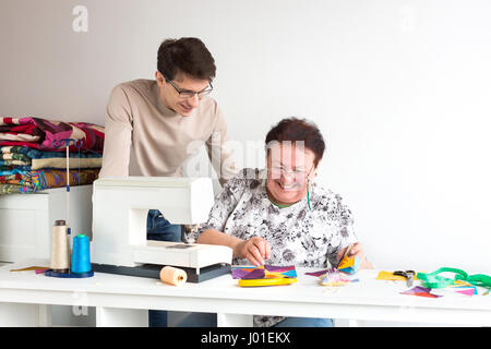 Patchwork und Quilten Schneider - Schneider zwei Lächeln bei der Arbeit im Studio, beugte sich über bunten Patchwork Tuch liegen auf dem Tisch neben dem Nähen m Stockfoto