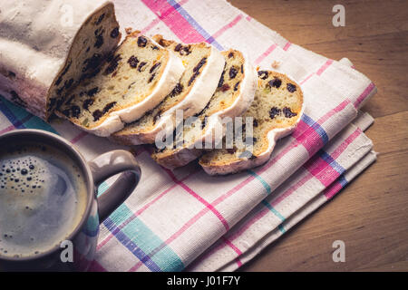 Christstollen, traditionelle deutsche Weihnachten Hefekuchen mit Rosinen, serviert mit einer Tasse Kaffee, dekoriert mit Tischdecke auf Holztisch Stockfoto