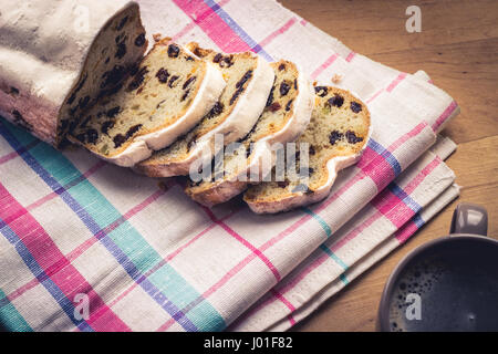 Christstollen, traditionelle deutsche Weihnachten Hefekuchen mit Rosinen, serviert mit einer Tasse Kaffee, dekoriert mit Tischdecke auf Holztisch Stockfoto