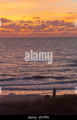 Silhouette eines Fischers mit Angeln Pol Angeln an einem Strand entlang des Golfs von Mexiko, wie er einen herrlich bunten Sonnenuntergang Uhren Stockfoto