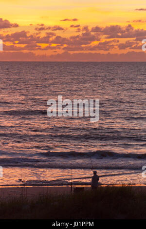 Silhouette eines Fischers mit Angeln Pol Angeln an einem Strand entlang des Golfs von Mexiko, wie er einen herrlich bunten Sonnenuntergang Uhren Stockfoto