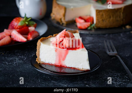 Käsekuchen mit frischen Erdbeeren und Erdbeer-Sirup auf schwarzen Druckplatte. Stockfoto