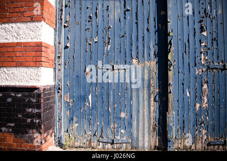 Shabby sets von Garage oder Fabrik Holztüren mit Peeling und blauen Farbe mit roten und weißen Backstein Spalten auf einem leeren Gebäude in Avonmouth verblasst Stockfoto