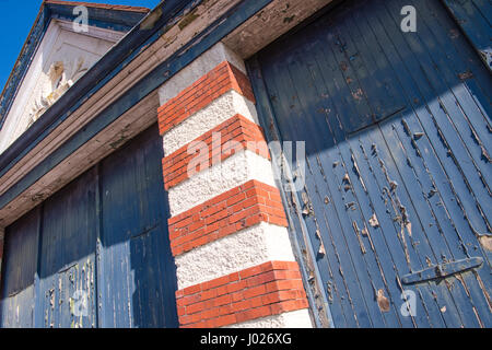 Shabby sets von Garage oder Fabrik Holztüren mit Peeling und blauen Farbe mit roten und weißen Backstein Spalten auf einem leeren Gebäude in Avonmouth verblasst Stockfoto
