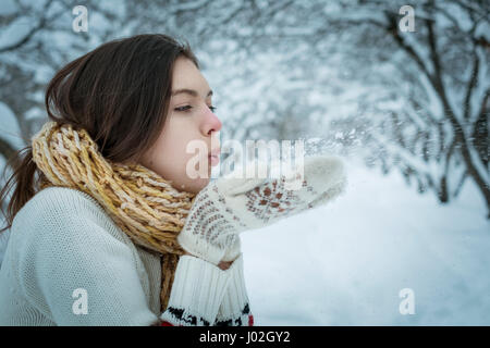 Das Mädchen ist warm angezogen, bläst aus Schnee aus Händen Stockfoto