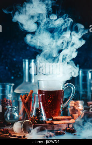 Dunkle Essen Foto mit dampfenden Tasse Kaffee, Gewürze, Anis und Zimt, in Laborumgebung mit Trichter, Becher und Reagenzgläser Stockfoto