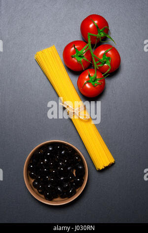 Ansicht von oben: Nudeln oder italienische Spaghetti, Tomaten und Oliven mit Zutaten auf schwarzem Stein Schiefer Hintergrund Stockfoto