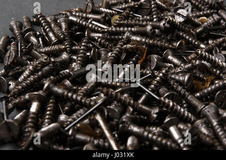 Techno-Hintergründe - schwarz geölt Haufen Schrauben auf einem dunklen grauen Karton Stockfoto