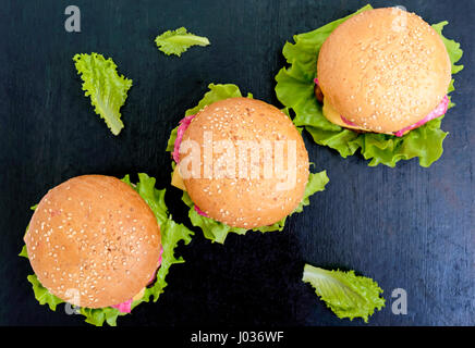 Hamburger mit grünen Salatblättern, saftige Schnitzel und einem weichen Brötchen mit Sesam auf dem schwarzen Hintergrund. Die Ansicht von oben Stockfoto