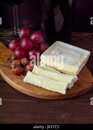 Ziegel geformt Käse mit weißen Schimmel, Haselnüsse, roten Trauben und Wein im Glas und Flasche Stockfoto