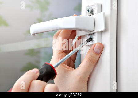 Eine Nahaufnahme der Schraubenzieher in der Hand, abschrauben der Schraube vom Griff des Fensterrahmens. Stockfoto