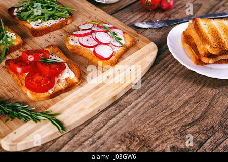 Vier Brötchen mit frischem Gemüse, Tomaten, Gurken, Radieschen und Rucola auf einem hölzernen Hintergrund. Selbst gemachter Butter und Toast. selektiven Fokus. Stockfoto