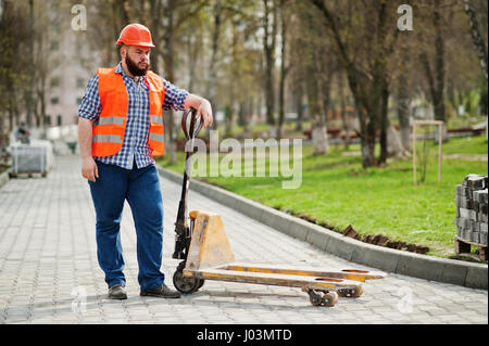 Brutale Bart Arbeiter Mann Anzug Bauarbeiter in orange-Schutzhelm mit Hubwagen. Stockfoto