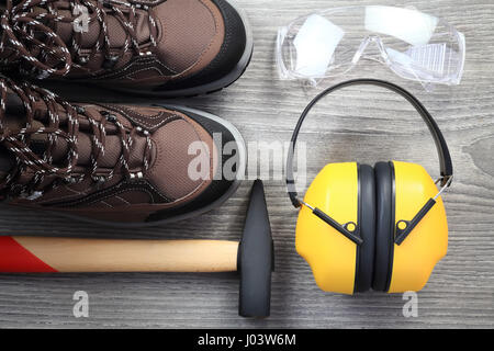 Arbeitsinstrumente und Kleidung auf hölzernen Hintergrund. Nahaufnahme der Schutzbrille und Kopfhörer von oben. Hammer mit Holzgriff. Neue Arbeit Schuhe cl Stockfoto