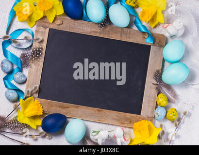 Ostern-Rahmen mit gemalten blauen Eiern, Blumen und leeren Tafel mit Textfreiraum Stockfoto