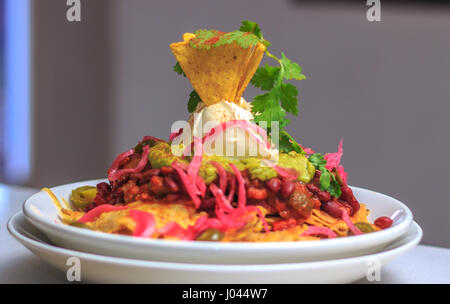 Würzige vegetarische Bohnen Nachos mit leckeren Käse-Mais-Chips, Sauerrahm, Guacamole, Avocado, Gurke, Jalapeños, Koriander Stockfoto