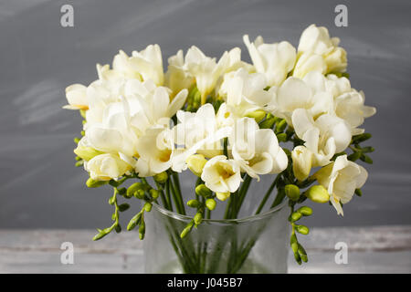 Weiße freesie Blumen in dekorativen Vase auf dem Hintergrund der grauen Wand Stockfoto