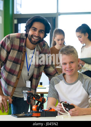 Schüler und Lehrer lächelnd in die Kamera in der Klasse. Sie arbeiten zusammen an einem Roboterarm. Stockfoto
