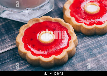 Makroaufnahme eines Cookies mit roten Kirschen Gelee. In der Nähe liegt ein Glas Milch. Süße Speisen Stockfoto