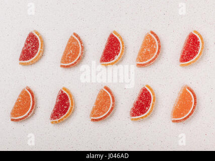Scheiben von Orangen und Grapefruits aus Marmelade in einem Muster in zwei Reihen auf einem grauen Hintergrund angelegt. Stockfoto