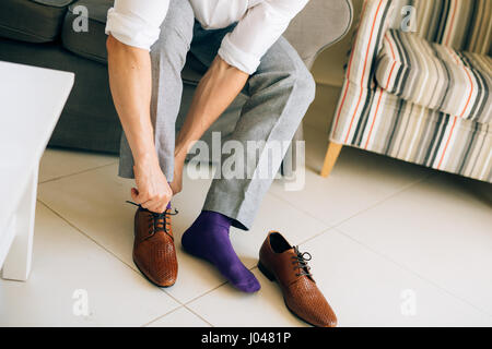 Der Mann im grauen Hosen und ein lila Kleid Strümpfe braune Schuhe mit Schnürung auf der Couch sitzen. Stockfoto