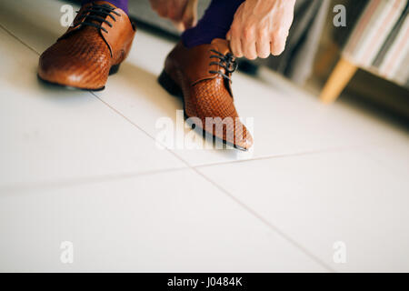 Der Mann im grauen Hosen und ein lila Kleid Strümpfe braune Schuhe mit Schnürung auf der Couch sitzen. Stockfoto