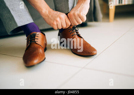 Der Mann im grauen Hosen und ein lila Kleid Strümpfe braune Schuhe mit Schnürung auf der Couch sitzen. Stockfoto