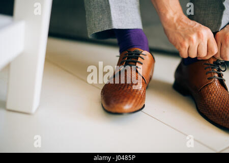 Der Mann im grauen Hosen und ein lila Kleid Strümpfe braune Schuhe mit Schnürung auf der Couch sitzen. Stockfoto