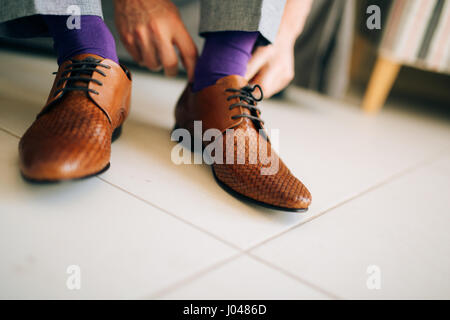 Der Mann im grauen Hosen und ein lila Kleid Strümpfe braune Schuhe mit Schnürung auf der Couch sitzen. Stockfoto