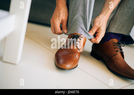 Der Mann im grauen Hosen und ein lila Kleid Strümpfe braune Schuhe mit Schnürung auf der Couch sitzen. Stockfoto