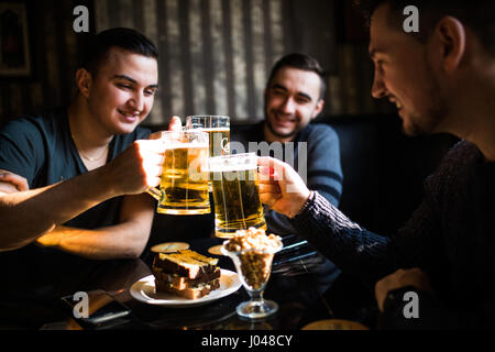 Menschen, Männer, Freizeit, Freundschaft und Feier Konzept - glücklich männlichen Freunden Bier trinken und Klirren der Gläser in Bar oder Kneipe Stockfoto