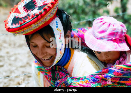 Nahaufnahme von Porträt eines lächelnden Quechua Frau in bunten traditionellen handgemachten Outfit gekleidet und ihr Baby im Tragetuch Stockfoto