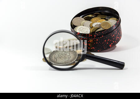 Silbermünze unter einer Lupe auf einem Hintergrund von einer Box mit Münzen Stockfoto