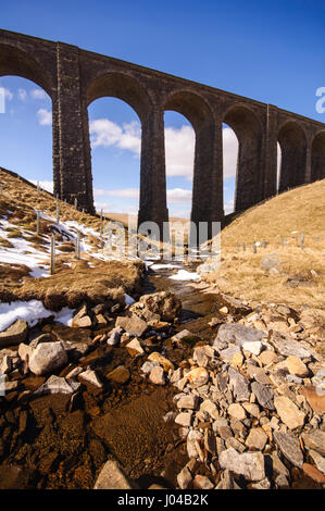 Die nachbarschaftlich Gill Viadukt auf der Settle Carlisle Eisenbahnlinie ist vor einem blauen Himmel oben Schnee gesprenkelt Mountain Stream des Kinds Gill Silhouette. Stockfoto