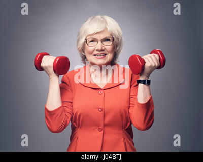 Lächelnde ältere Dame mit Hanteln auf grauem Hintergrund Stockfoto