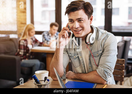 Fröhlicher junger Mann sitzt im café Stockfoto