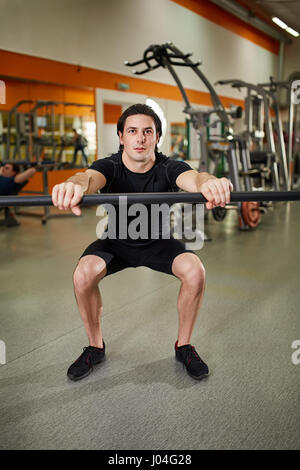 Junger sportlicher Mann im schwarzen Sportwear mit Bar der Langhantel beugen Muskeln im Fitness-Studio. Stockfoto