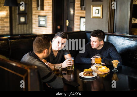 Treffen in der Kneipe. Drei glückliche Freunde trinken Bier in der Kneipe Stockfoto