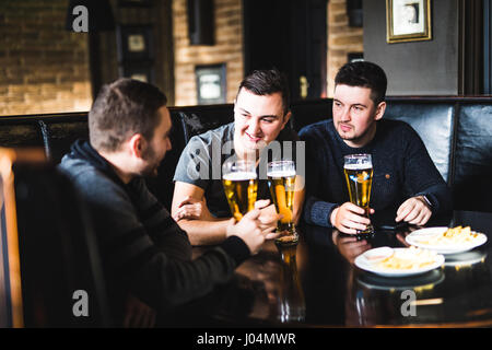 Drei junge Männer in Freizeitkleidung sind reden, Essen Chips und Bier zu trinken, während Sie sitzen im Pub, Nahaufnahme Stockfoto