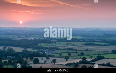 Die untergehende Sonne wirft einen roten Himmel durch staubige Schleier über der Flickenteppich der Molkerei Weiden, Feldern und Wäldern, die die ländliche Blackmore val Stockfoto